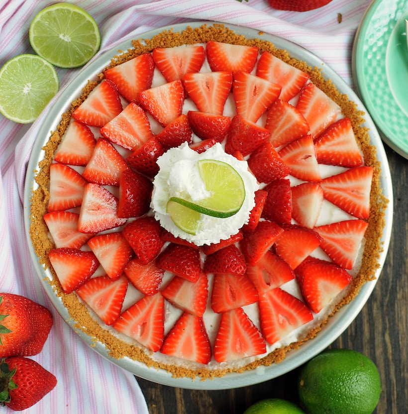 Picture of a cheesecake on a table with lime and strawberry