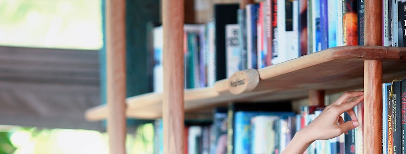 A lady reaches up to a library shelf's books