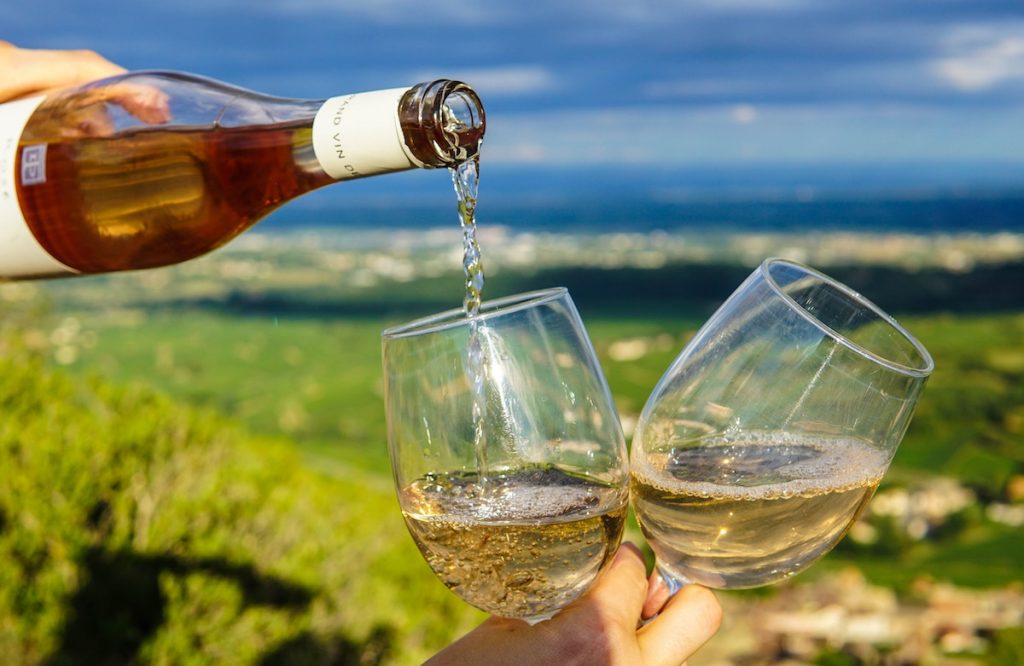 Pouring white wine into two glasses with a good view in background of fields