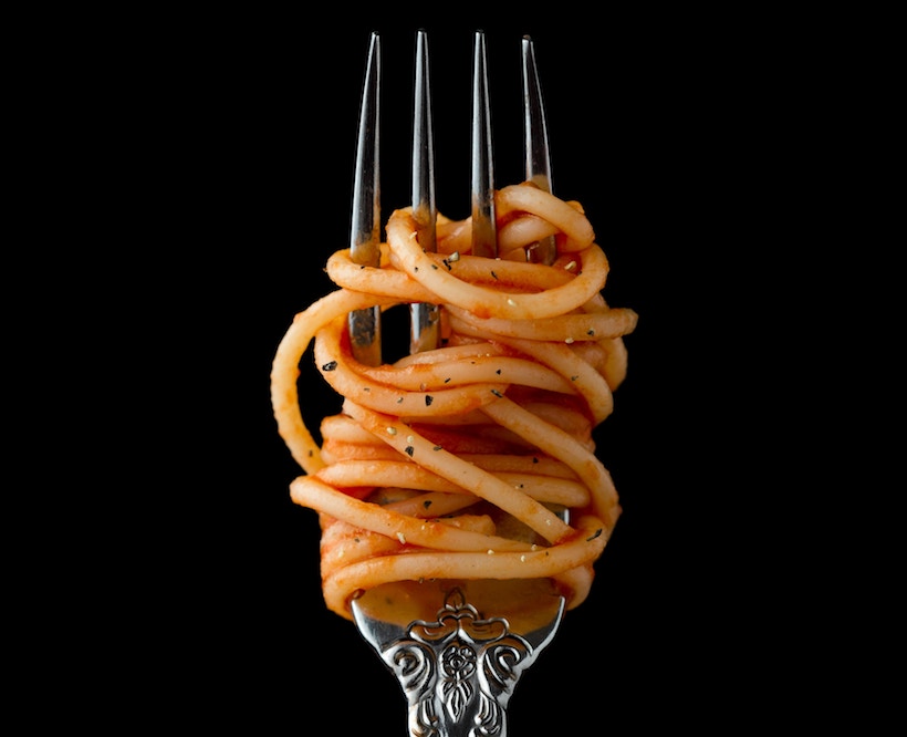 Spaghetti on a fork with sauce and herbs