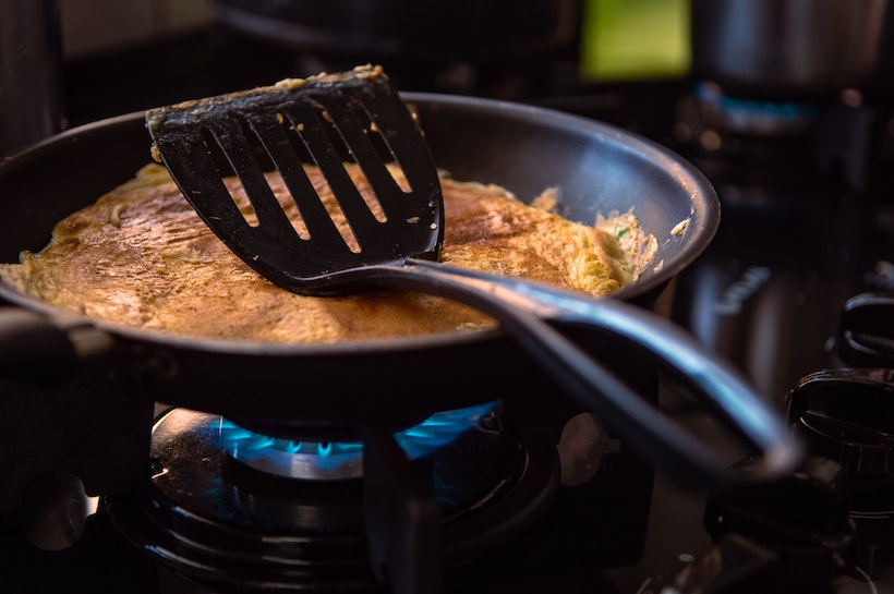 Black spatula in a frying pan over a gas flame