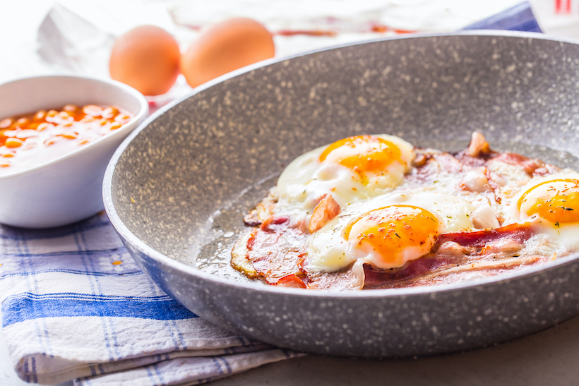 Ham and Eggs. Bacon and Eggs frying on ceramic pan. Salted egg and sprinkled with red pepper. English breakfast