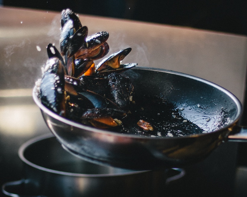 Clams being tossed in a black pan