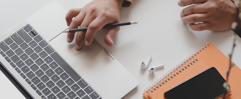 Man holding a pen with a leather notebook and laptop