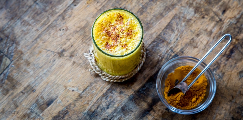 Turmeric in a dish next to a drink that's yellow with turmeric added