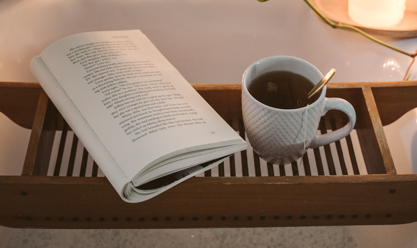 Cup of tea and an open book held over a tub with a candle