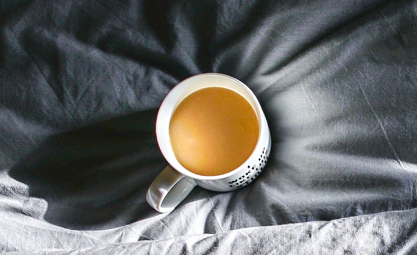 A coffee mug with creamer sitting on grey sheets