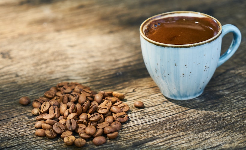 Coffee cup next to coffee beans on wooden table