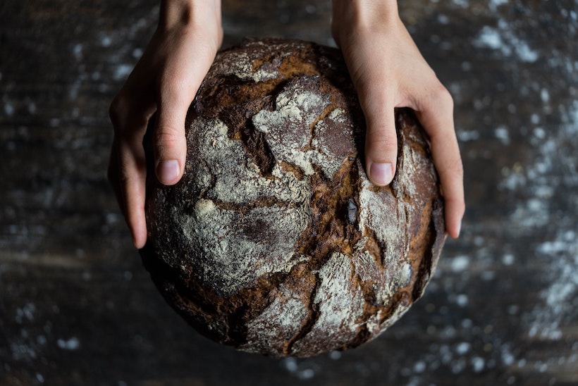 Lady holds round dark bread she baked