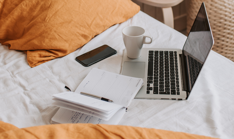 Laptop in bed with coffee and notebook and phone