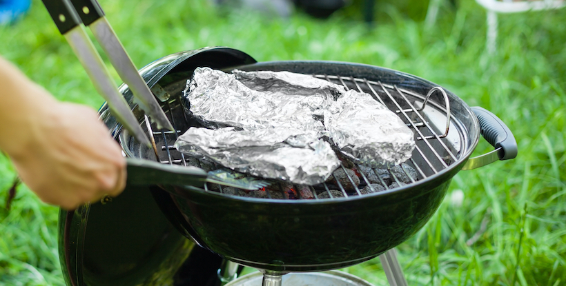 Grilling meat with barbecue an tin foil and tongs. Horizontal close up shot with a selective focus