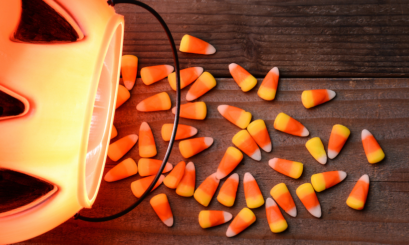 Plastic pumpkin and candy corn spill on a rustic wood background