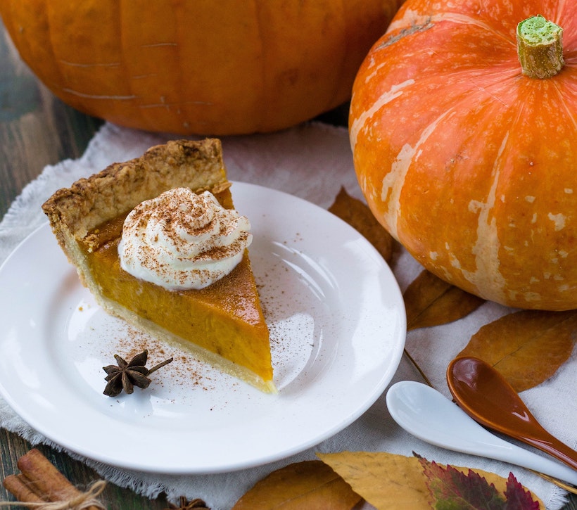 Pumpkin pie with cream and spice next to a pumpkin