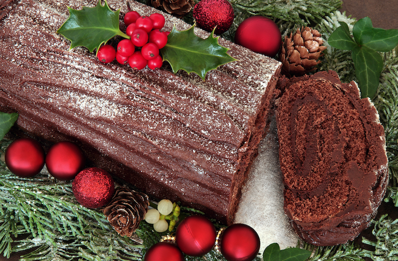 Chocolate yule log cake with red bauble decorations, holly, ivy, and mistletoe